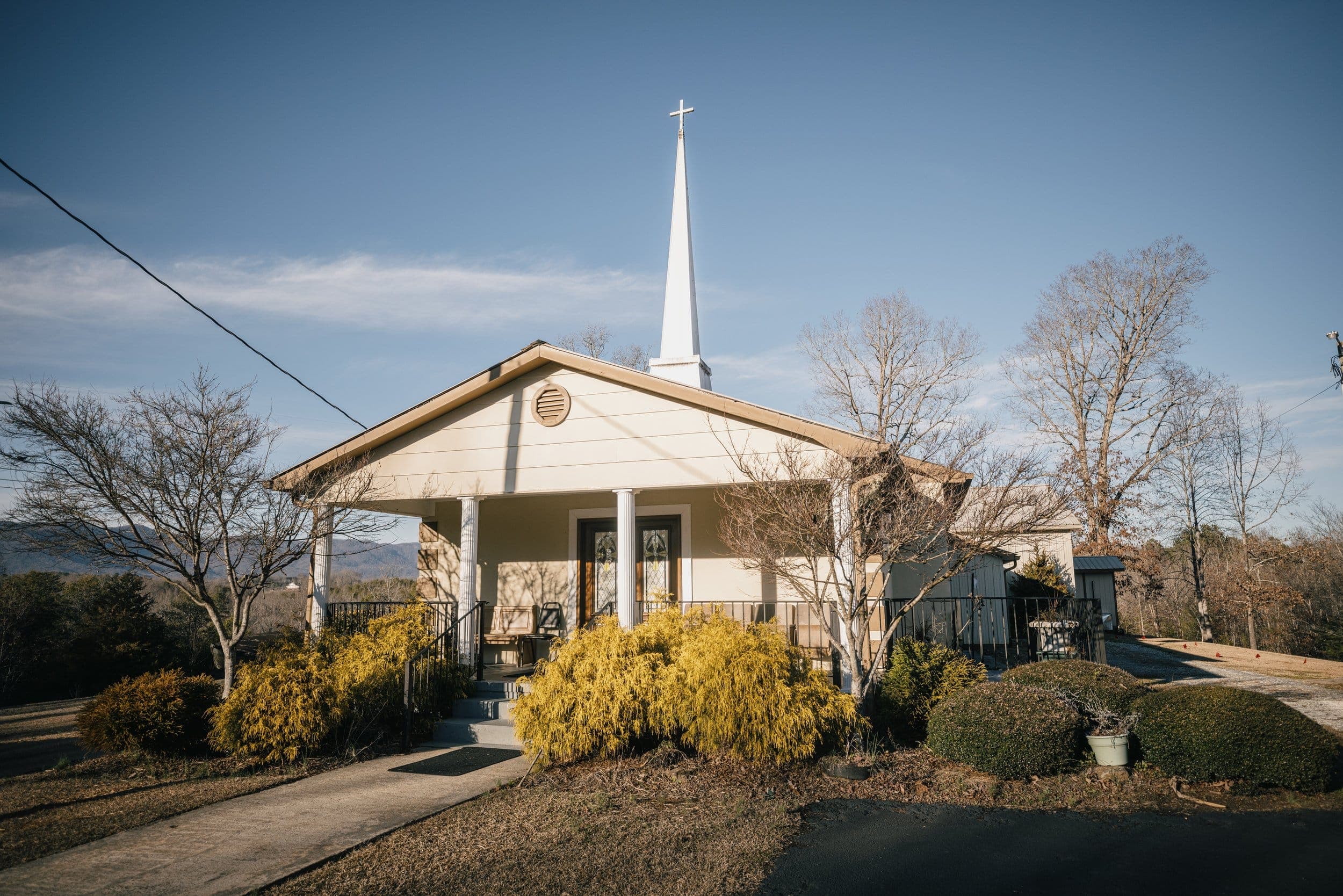 Front view of Soapstone Baptist Church, a white clapboard building with a steeple and cross, on a clear day