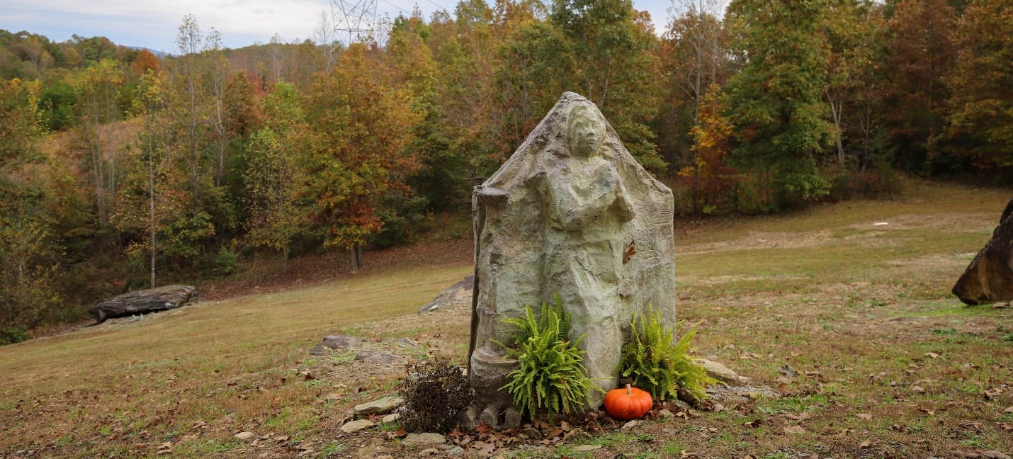 The "Praying Women" sculpture, a carved stone figure set among ferns on the grounds