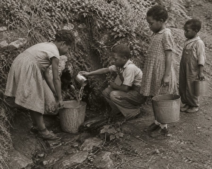 A historic photograph of children gathering water from the spring with metal buckets